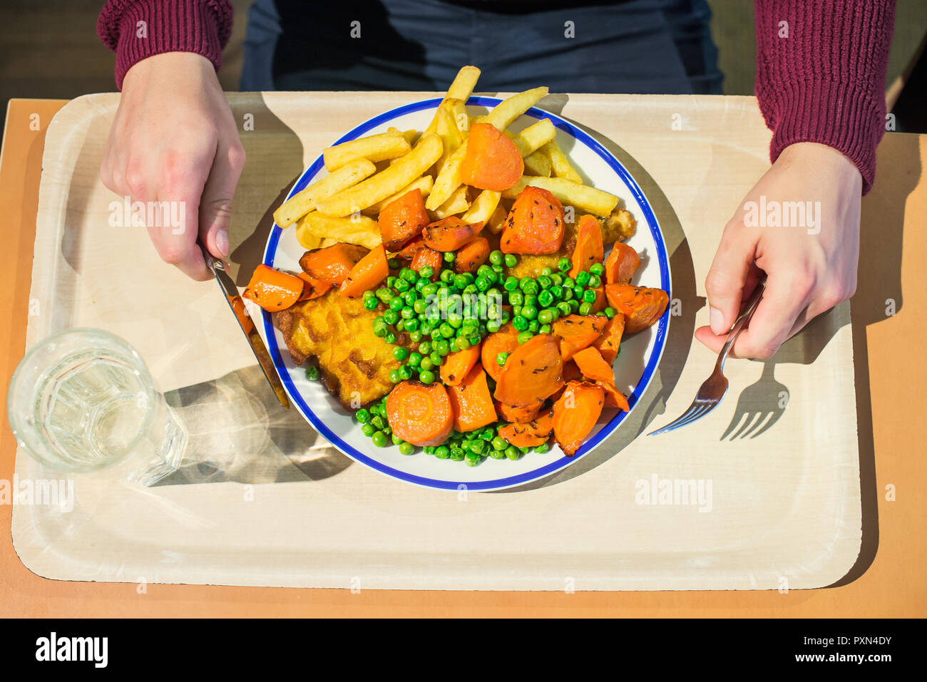 Man holding couverts et manger un plat traditionnel anglais - fish and chips avec petits pois, carottes cuites et de tartre sause. Restauration rapide, café lun d'affaires Banque D'Images