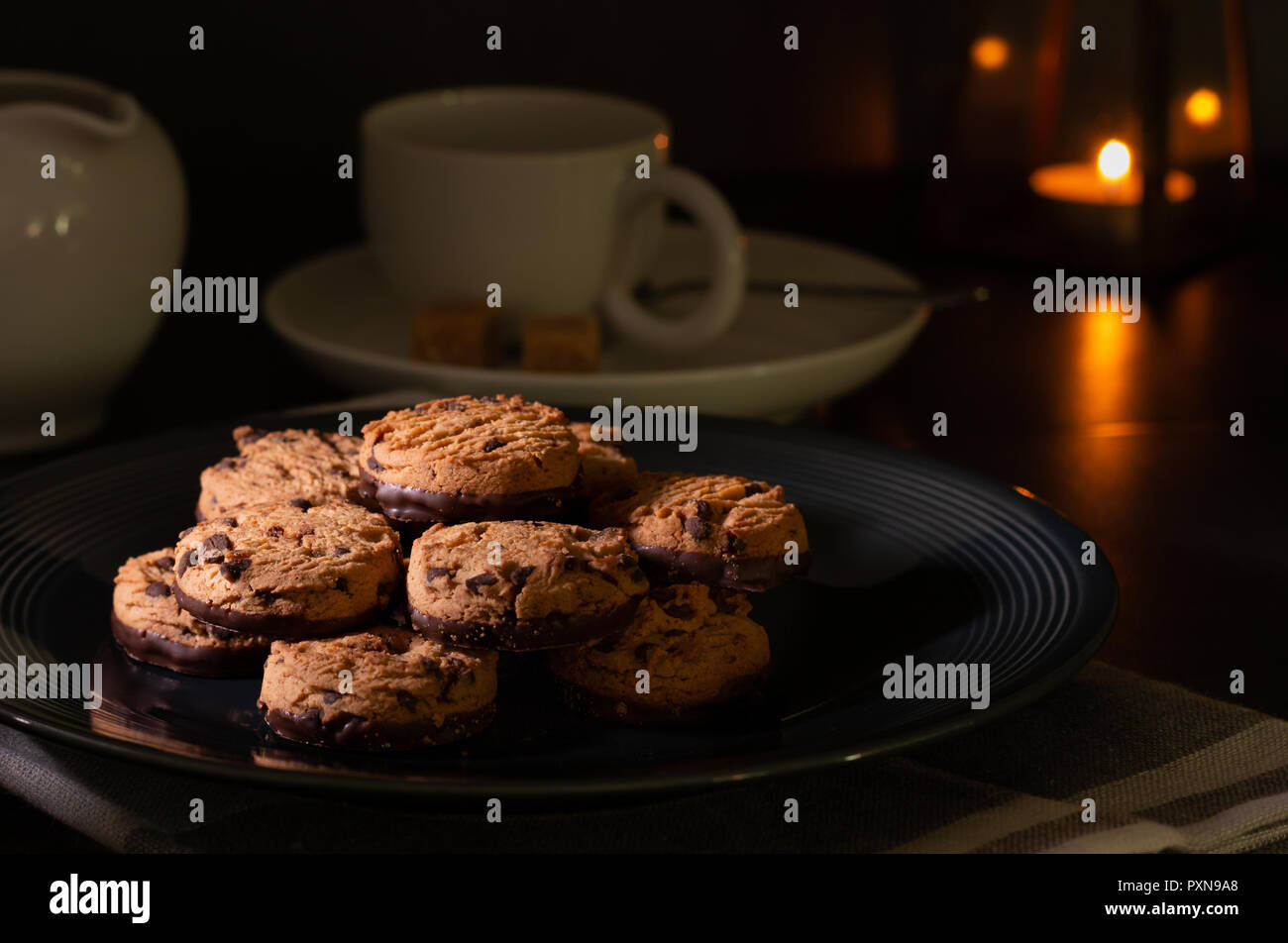 Cookies aux pépites de chocolat fait maison sur une table de cuisine avec du lait, chocolat noir et une tasse de café. Banque D'Images