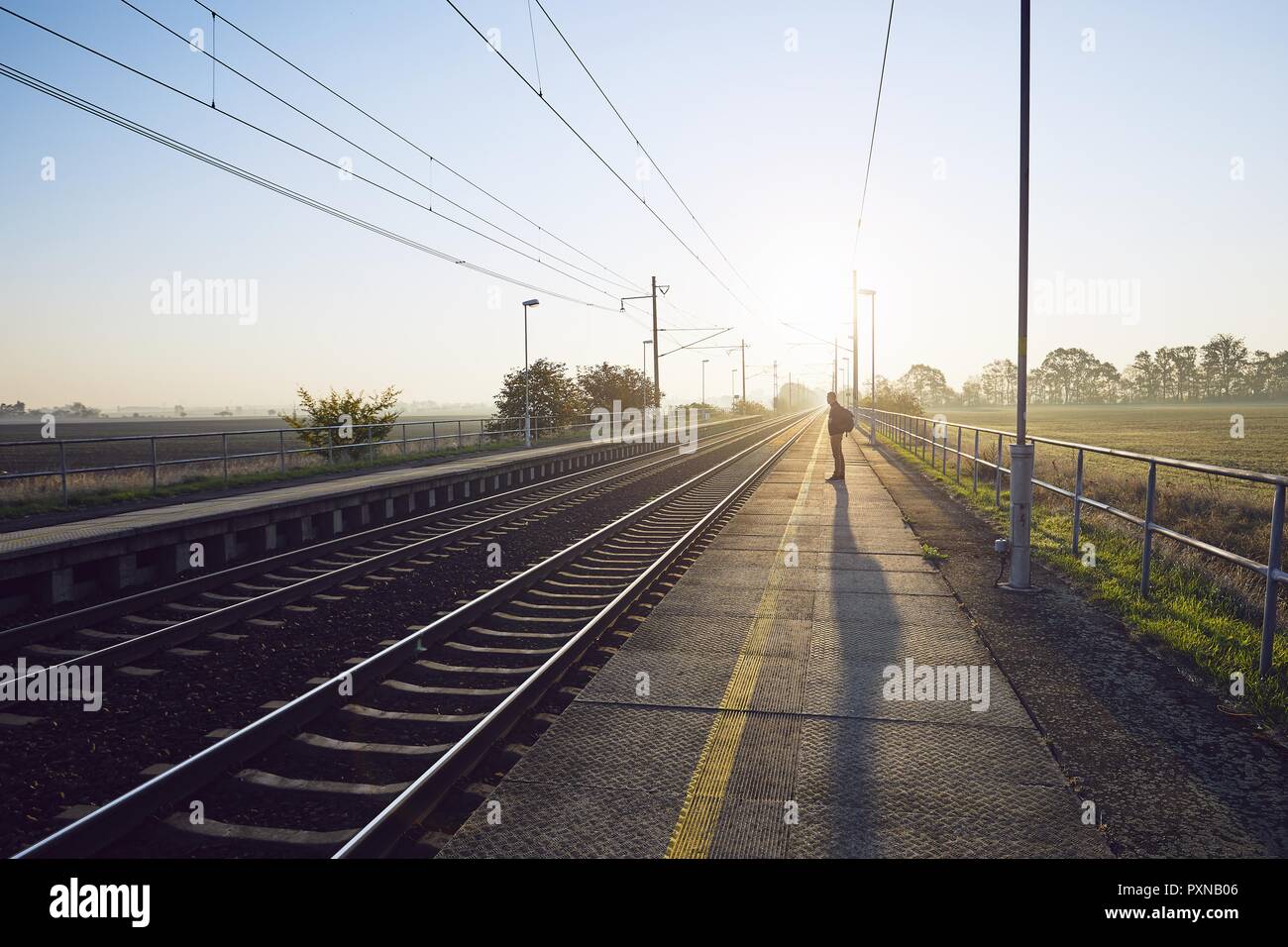 Jeune homme seul avec sac à dos en attente de train à la station de chemin de fer au lever du soleil. Banque D'Images