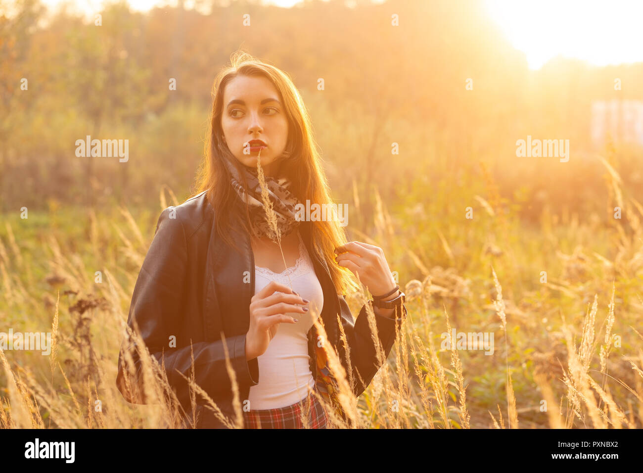 Belle jeune femme triste marche à l'herbe sèche, heure du coucher de soleil. Banque D'Images