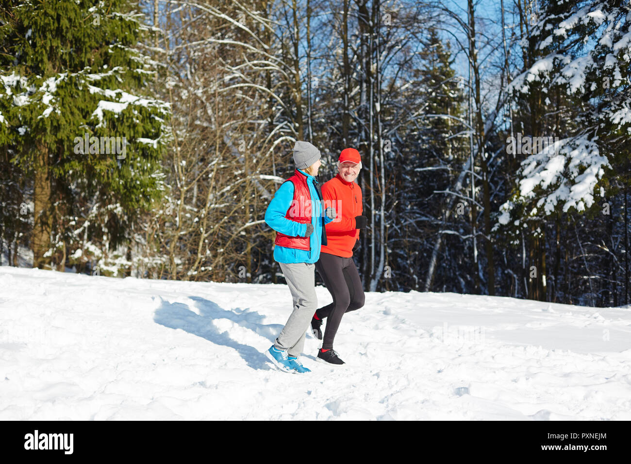 Senior conjoints ayant l'entraînement sportif sur l'hiver au chaud jour chez firtrees in snow Banque D'Images