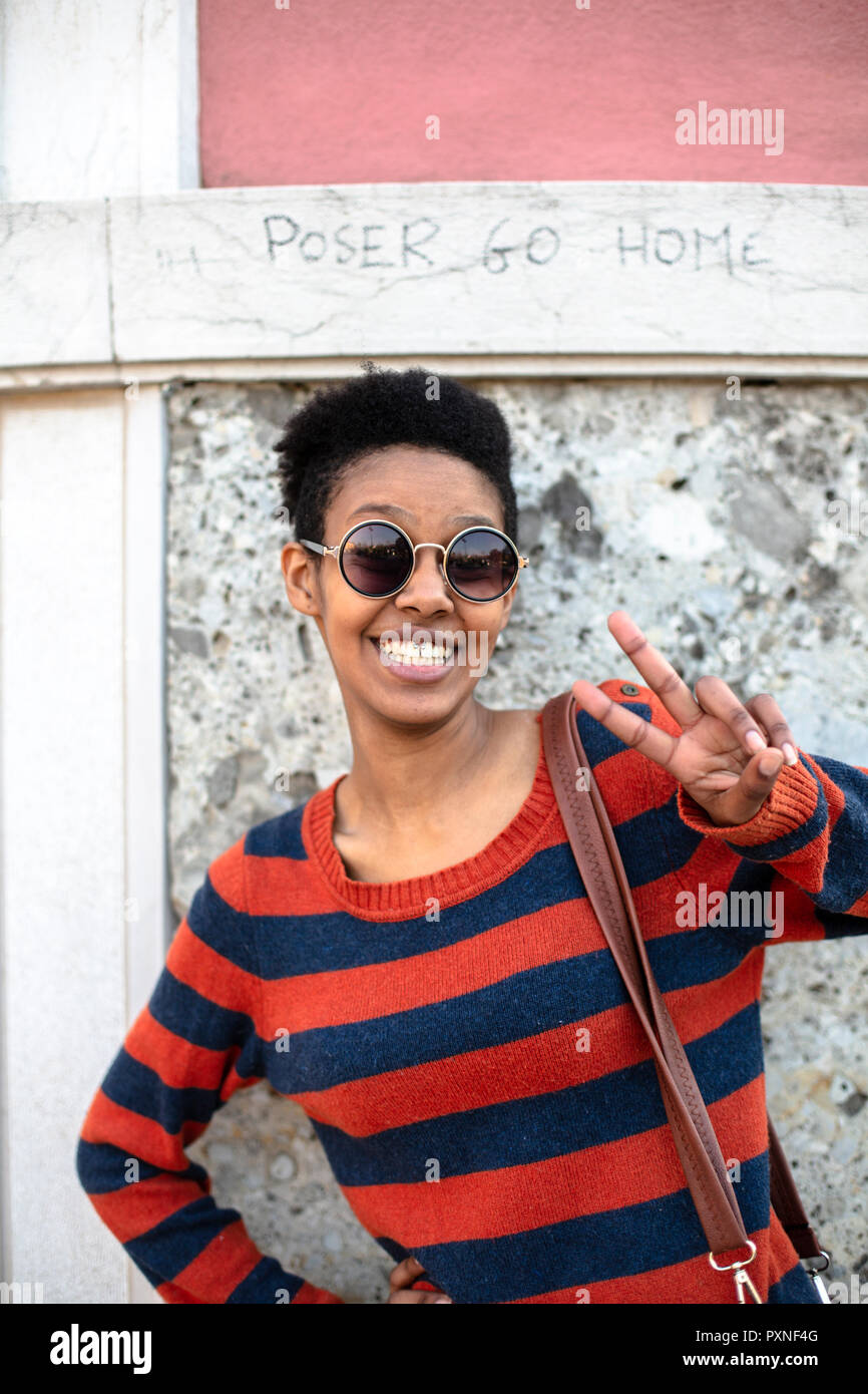 Portrait de jeune femme portant des lunettes et pull rayé montrant la victoire Banque D'Images
