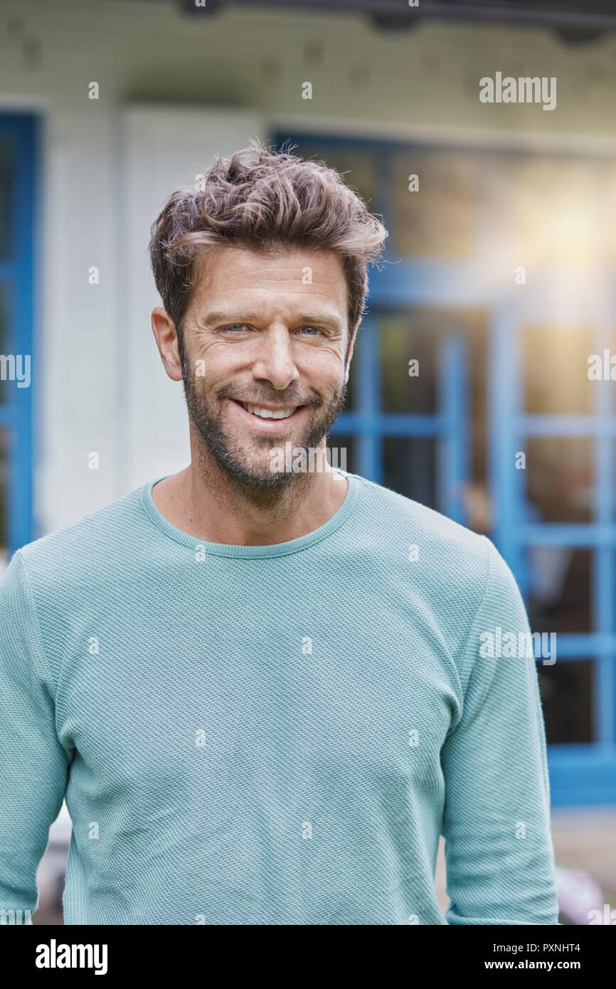 Portrait of smiling man in front of house avec fenêtre bleu Banque D'Images