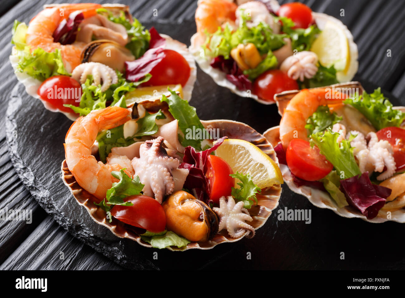 Salade de fruits de mer sains diététiques de crevettes, poulpe bébé, moules, calmars et les pétoncles avec légumes en coquilles de mer gros plan sur un tableau noir. horizonta Banque D'Images