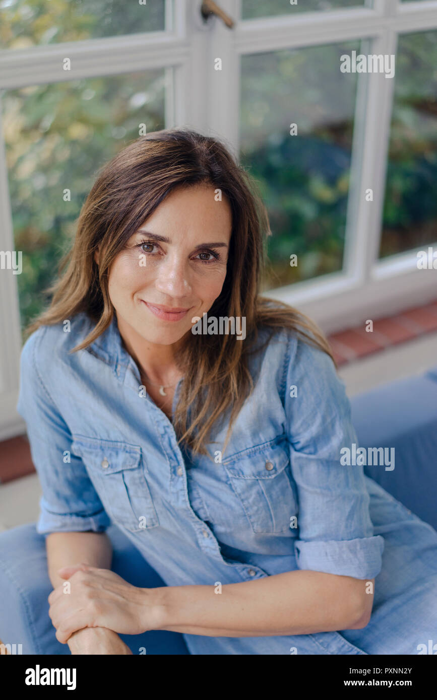 Portrait of smiling mature woman sitting on sofa at home Banque D'Images