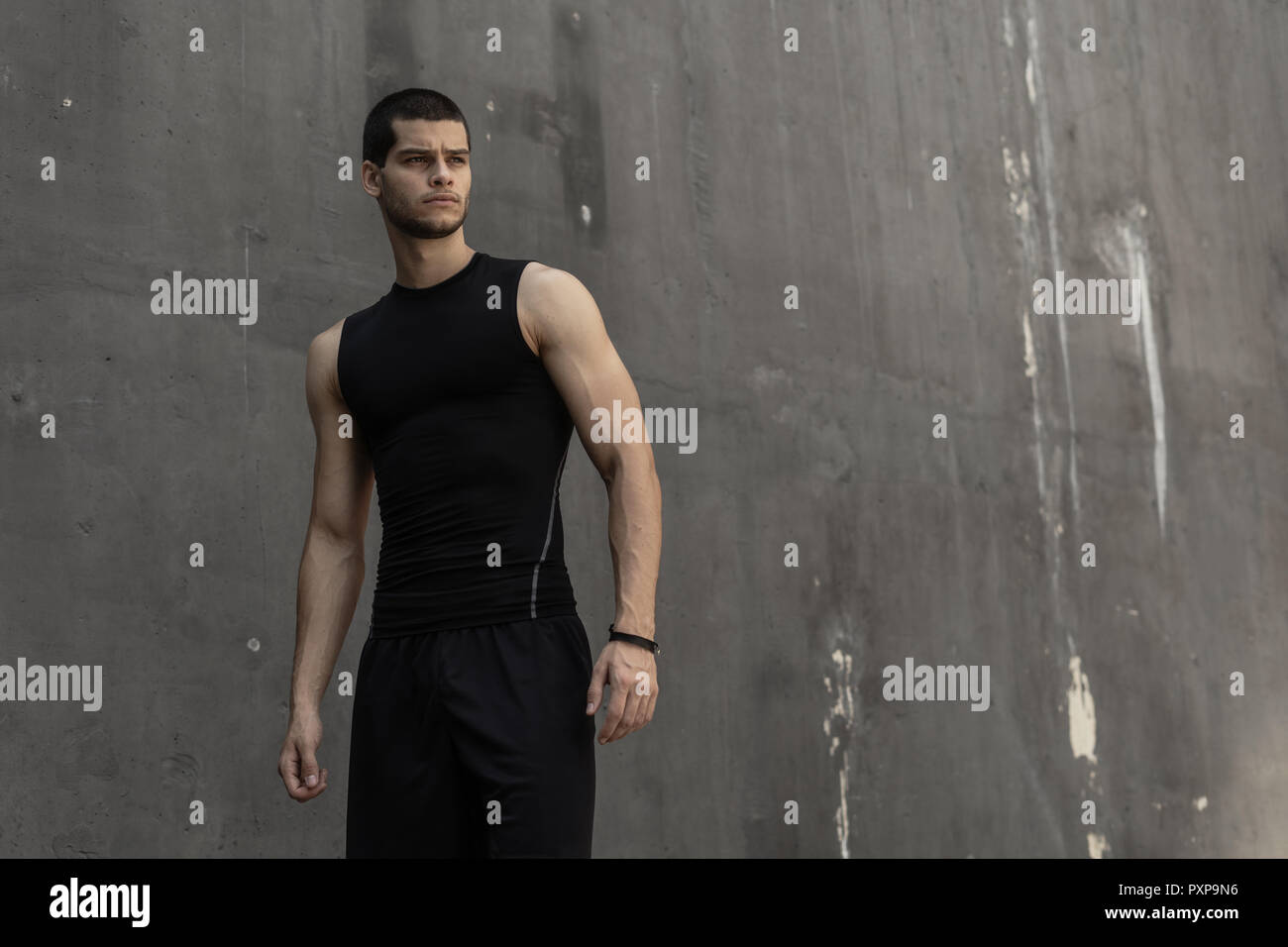 Portrait de jeune homme musclé athlétique, dans les vêtements de sport, posant sur l'arrière-plan industriel gris. Hauteur à la mode homme, un modèle sportif, corps musclé s Banque D'Images