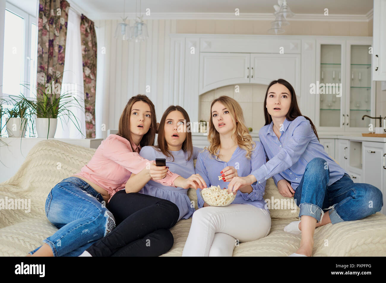 Les jeunes filles de regarder la télévision, eating popcorn assis sur le canapé. Banque D'Images