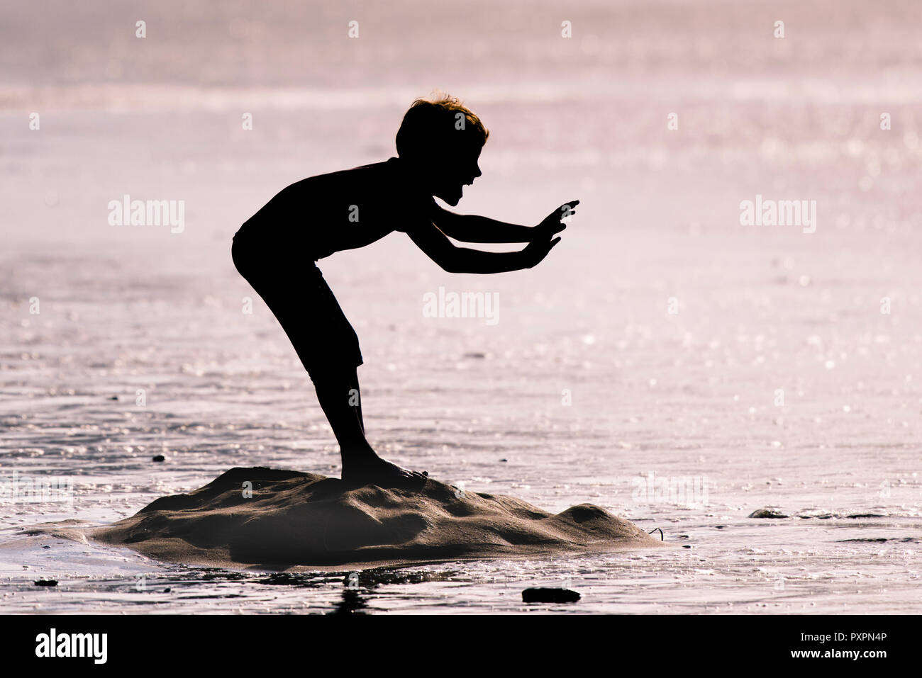 La silhouette d'un jeune garçon d'essayer d'arrêter la mer sur la plage de Fistral entrant dans Newquayin Cornwall. Banque D'Images