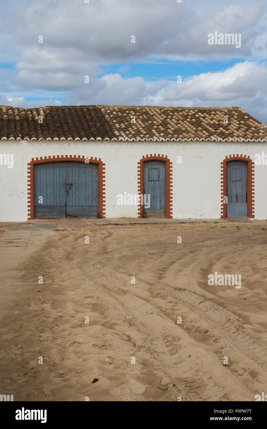 La façade blanche de l'immeuble avec portes en bois bleu et cadres formés de briques orange. Toit de tuiles multicolores. Route de sable. Ciel d'automne nuageux. Tavira, Banque D'Images