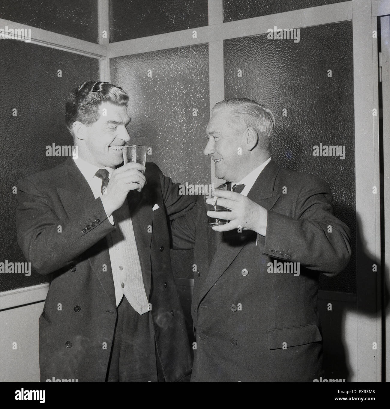 1956, historiques, à l'intérieur d'une chambre à Millwall FC, le président avec un verre et de cigarettes dans la main se félicite de la nouvelle manager du club, Ron Gray, qui a aussi le verre dans la main, Millwall Football Club, New Cross, London, SE14, England, UK. Banque D'Images