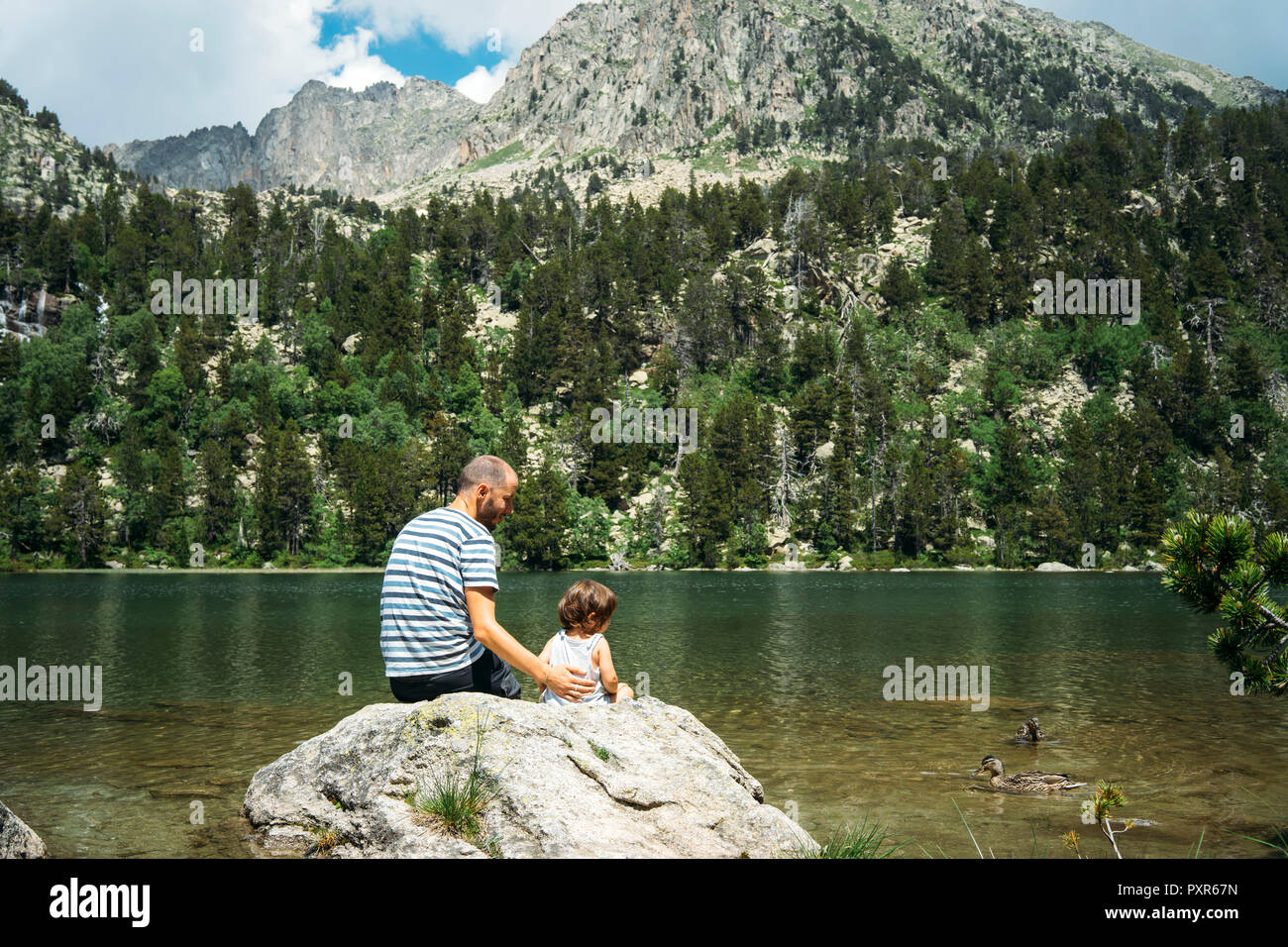 L'Espagne, le père et la fille assise sur un rocher à un lac de montagne, l'alimentation des canards Banque D'Images