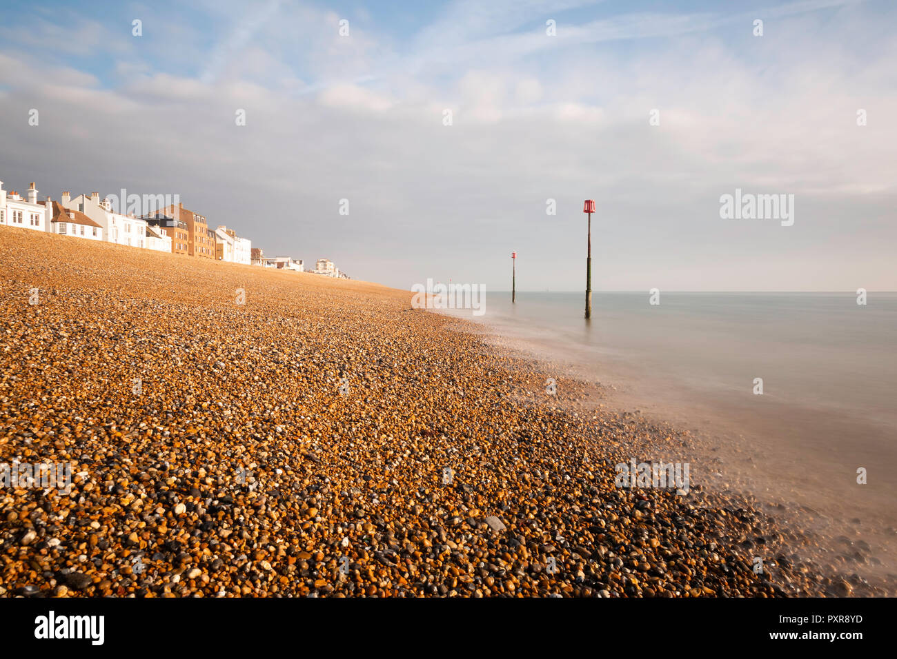 Début de la lumière du matin sur la plage de galets à Deal, Kent, UK. Les maisons le long de la rue de plage sont visibles et il y a des marqueurs de marée dans la mer. Banque D'Images