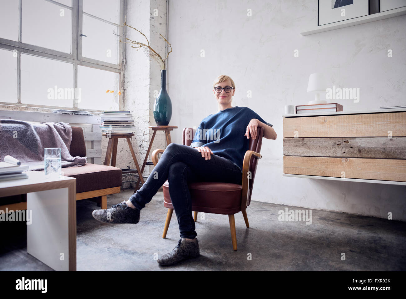 Smiling woman sitting on chair in loft à bras Banque D'Images