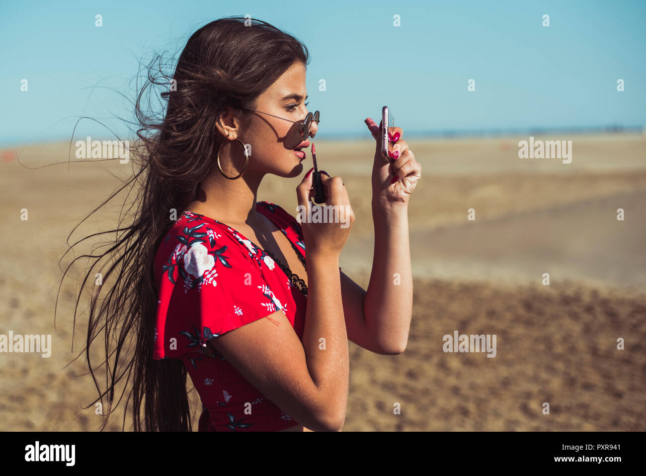 Teenage girl appliquant un brillant à lèvres sur la plage Banque D'Images