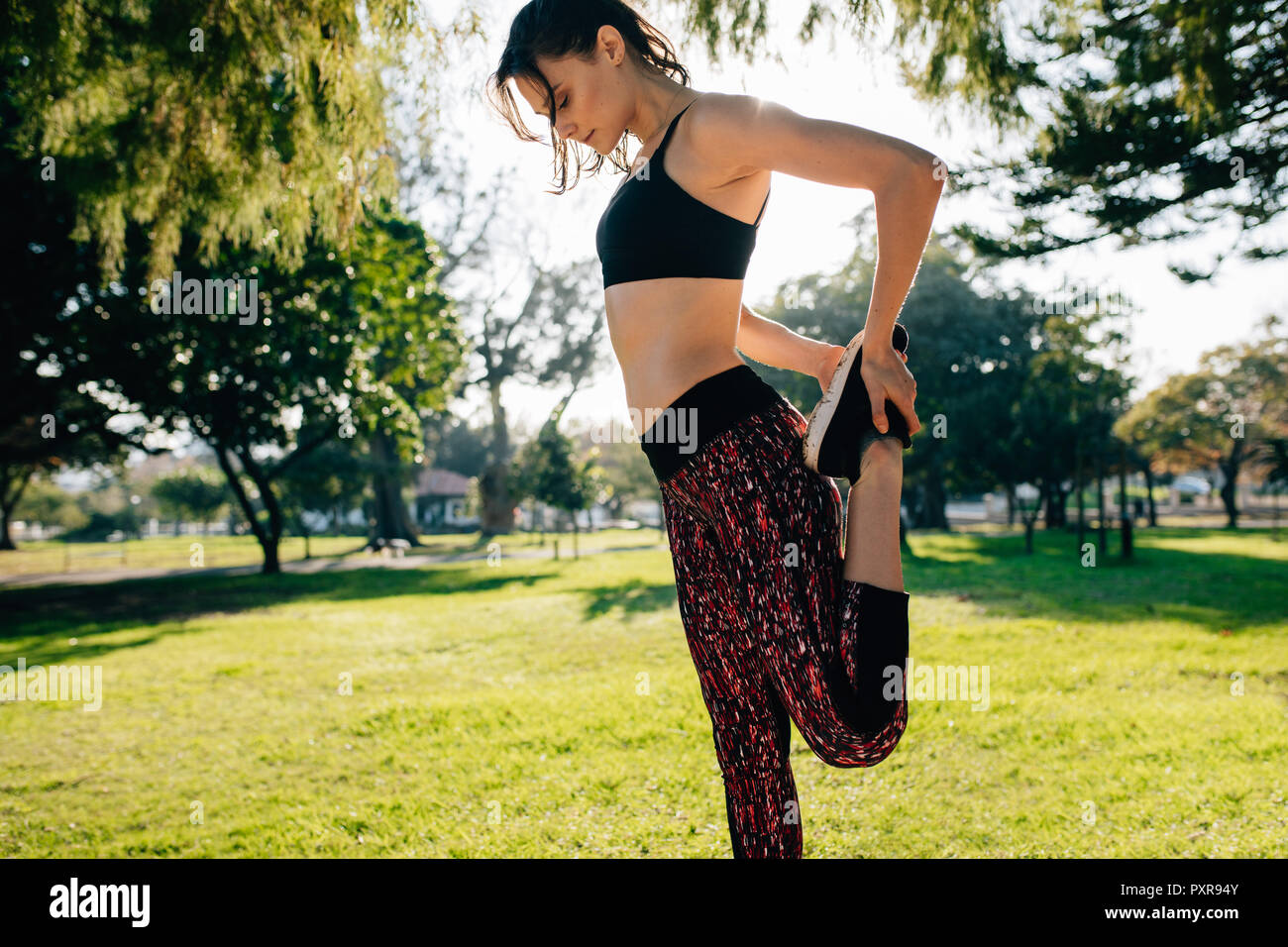 Vue latérale du sportswear féminin dans l'article dans le parc et d'étirement des muscles des jambes avant l'entraînement. Les femmes exerçant dans le parc le matin. Banque D'Images