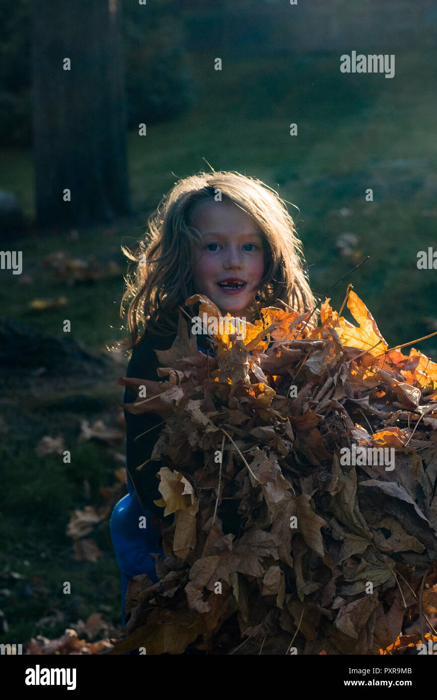 Jeune garçon aux cheveux longs à jouer avec l'automne feuilles d'érable Banque D'Images