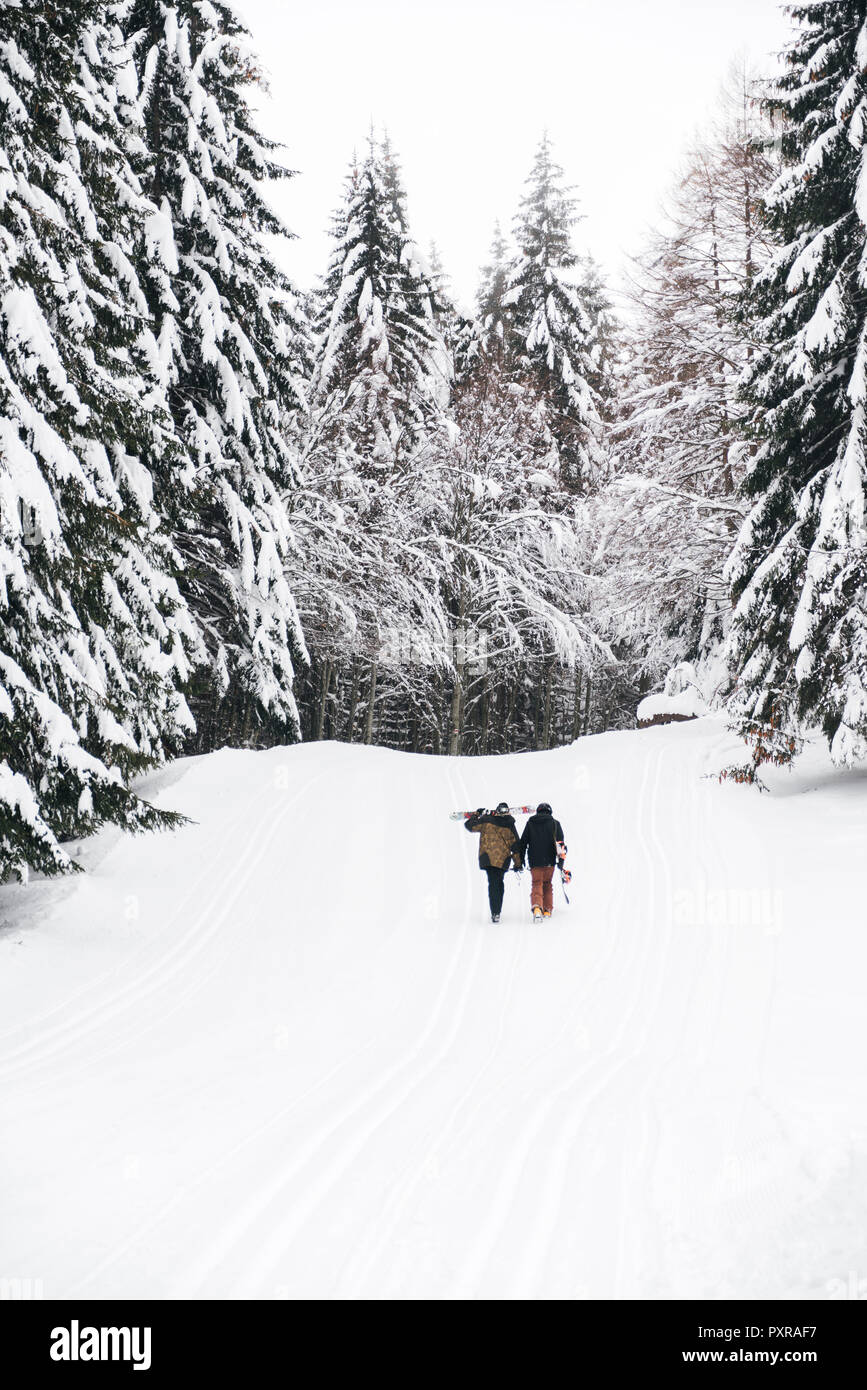 L'Italie, Modena, Cimone, vue arrière du couple avec ski et snowboard randonnée en forêt d'hiver Banque D'Images