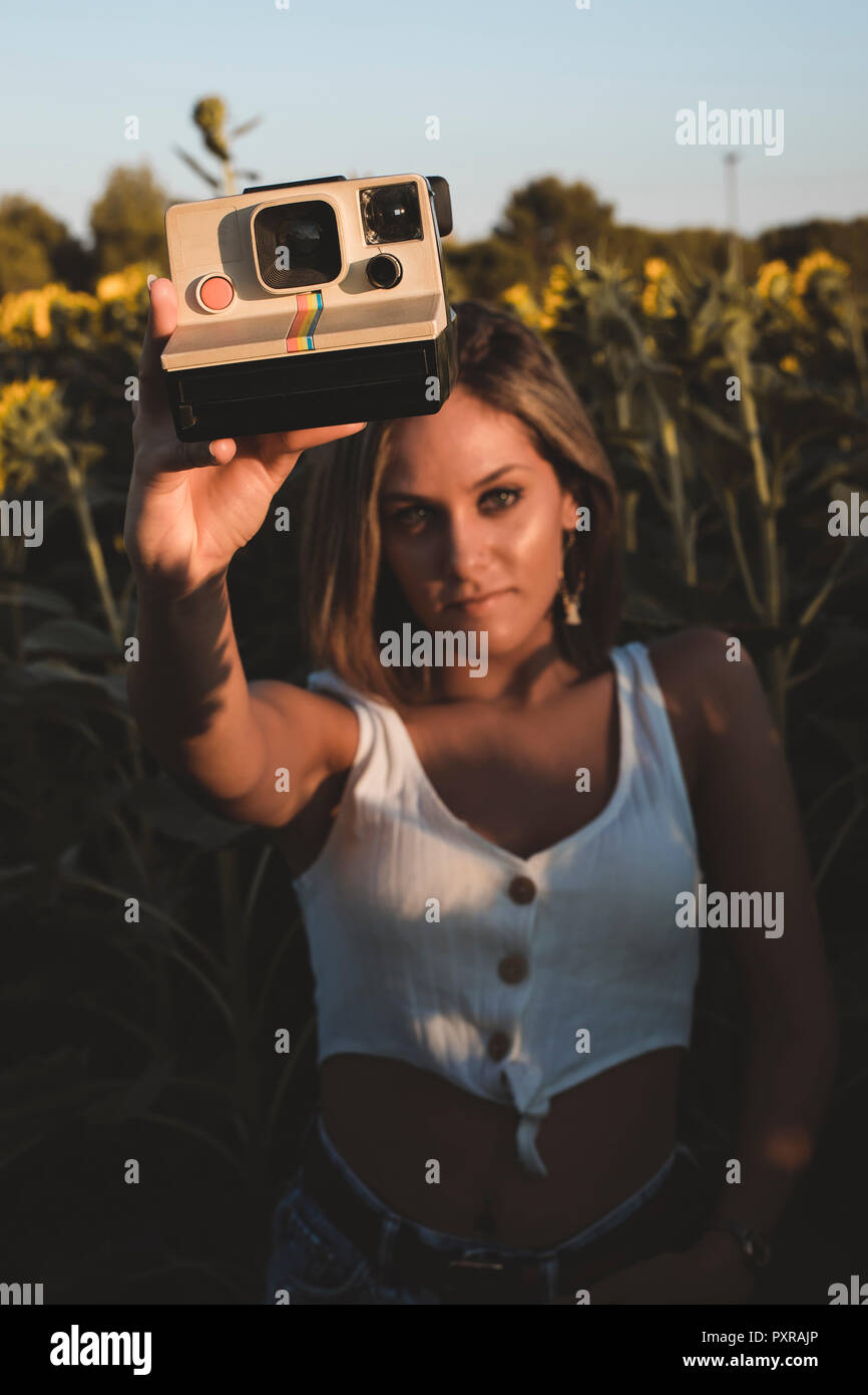 Jeune femme dans un champ de tournesols tenant un appareil photo instantané Banque D'Images