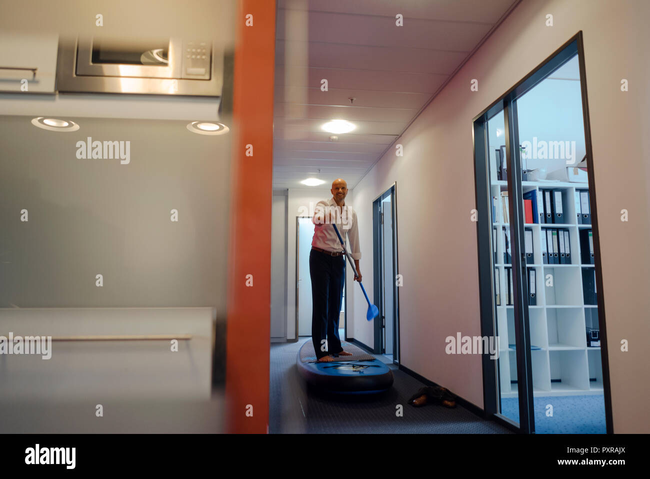 Businessman standing on paddle board, l'exercice in office corridor Banque D'Images