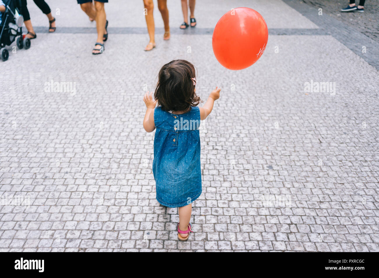 Vue arrière de baby girl with red balloon, marcher sur la chaussée Banque D'Images