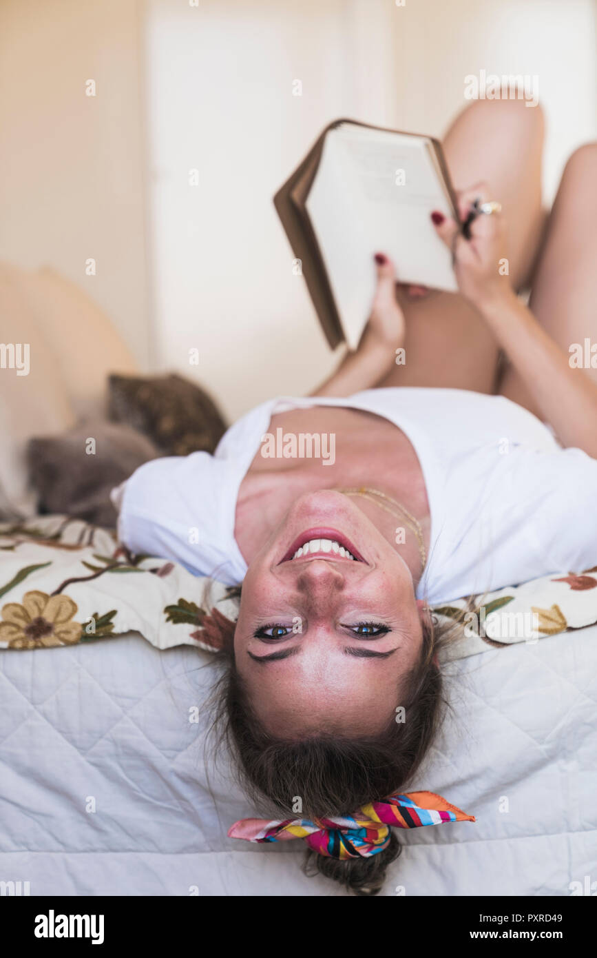 Portrait of happy young woman lying on bed at home avec diary Banque D'Images