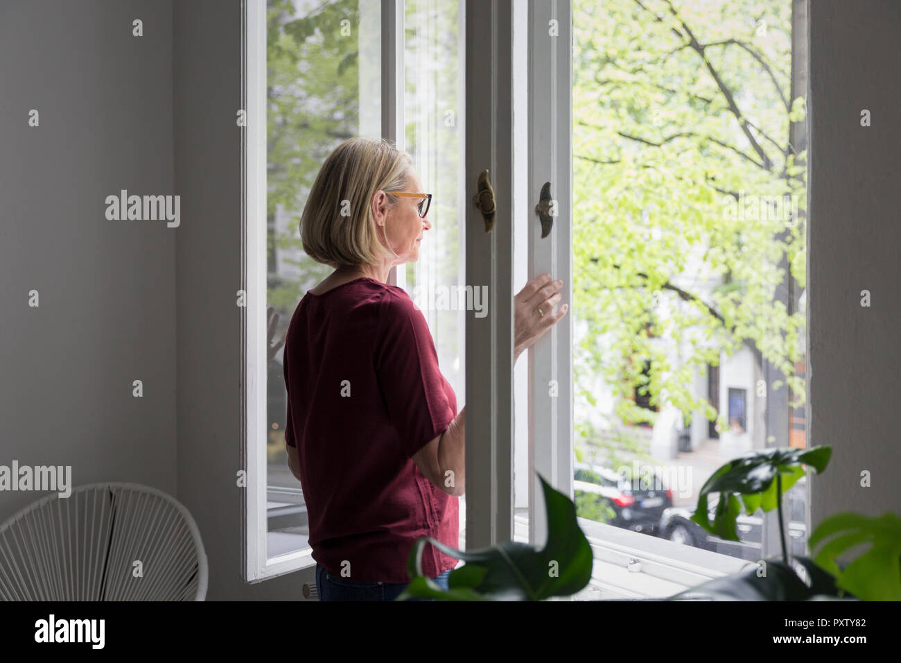 Femme mature à l'ouverture de la fenêtre Banque D'Images