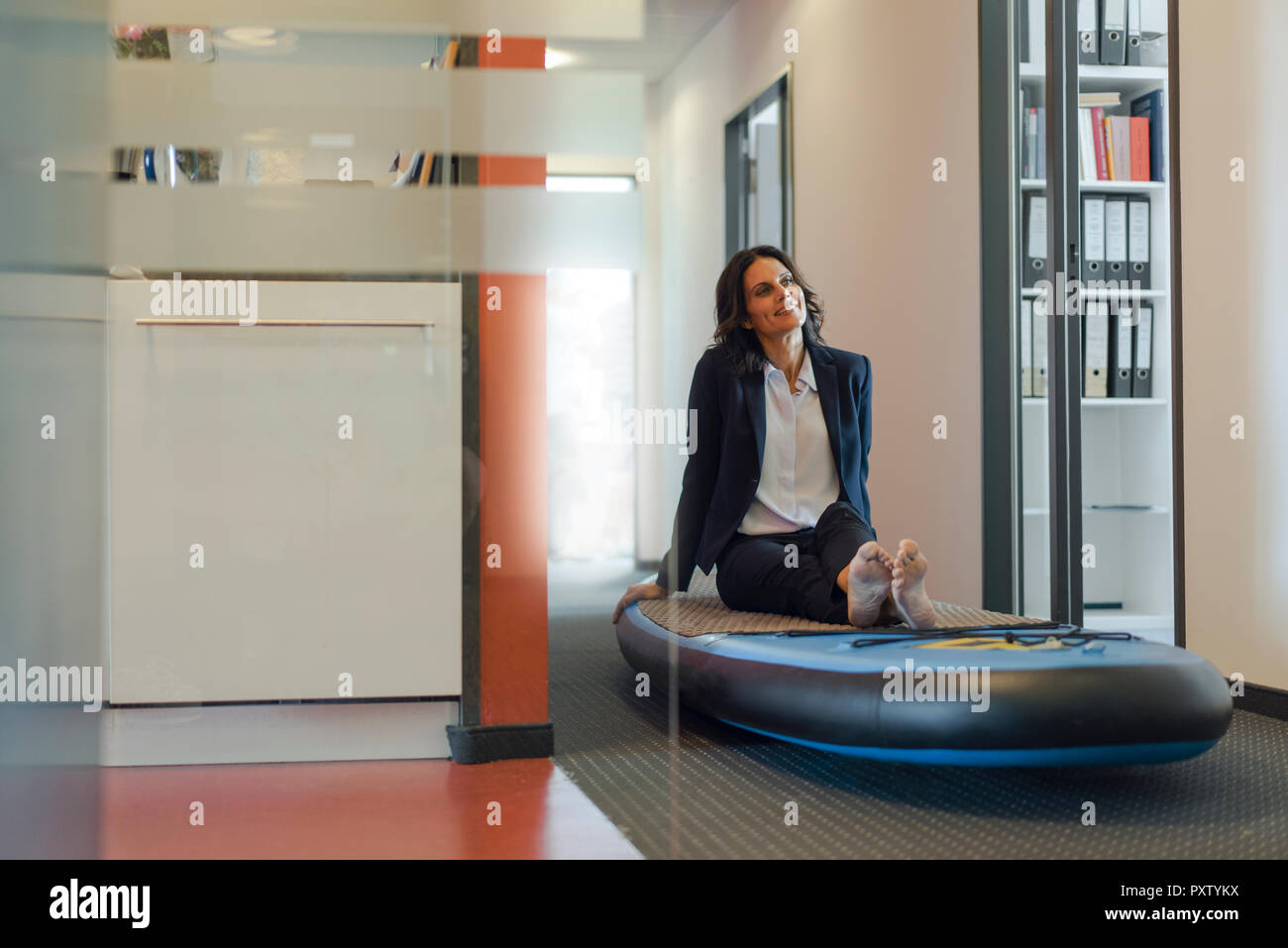 Businesswoman sitting on paddle board, daydreaming in office Banque D'Images