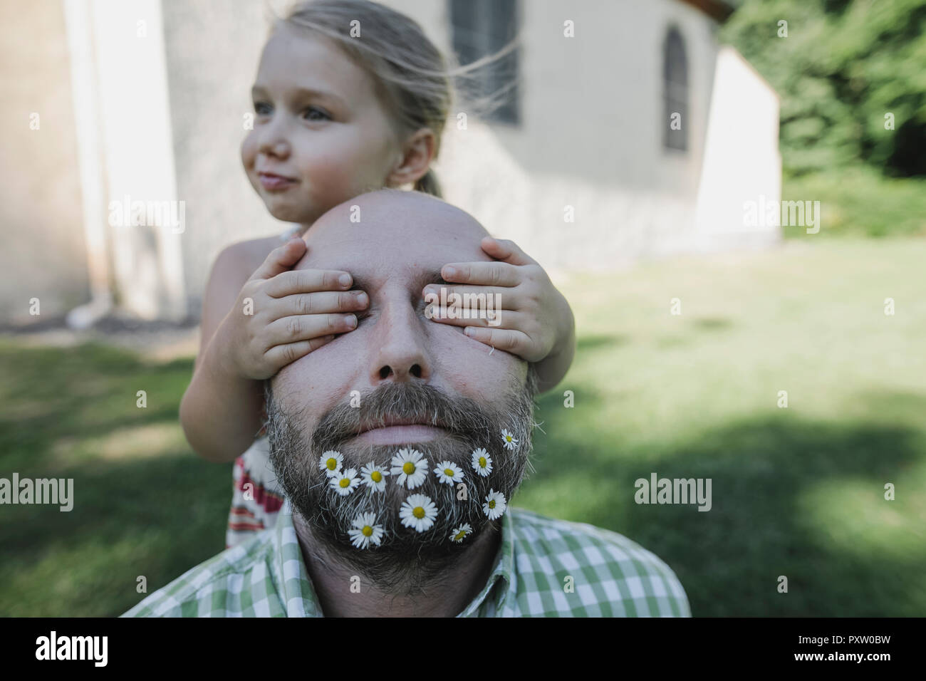 Little girl's hands couvrant les yeux de l'homme mûr avec marguerites dans sa barbe Banque D'Images