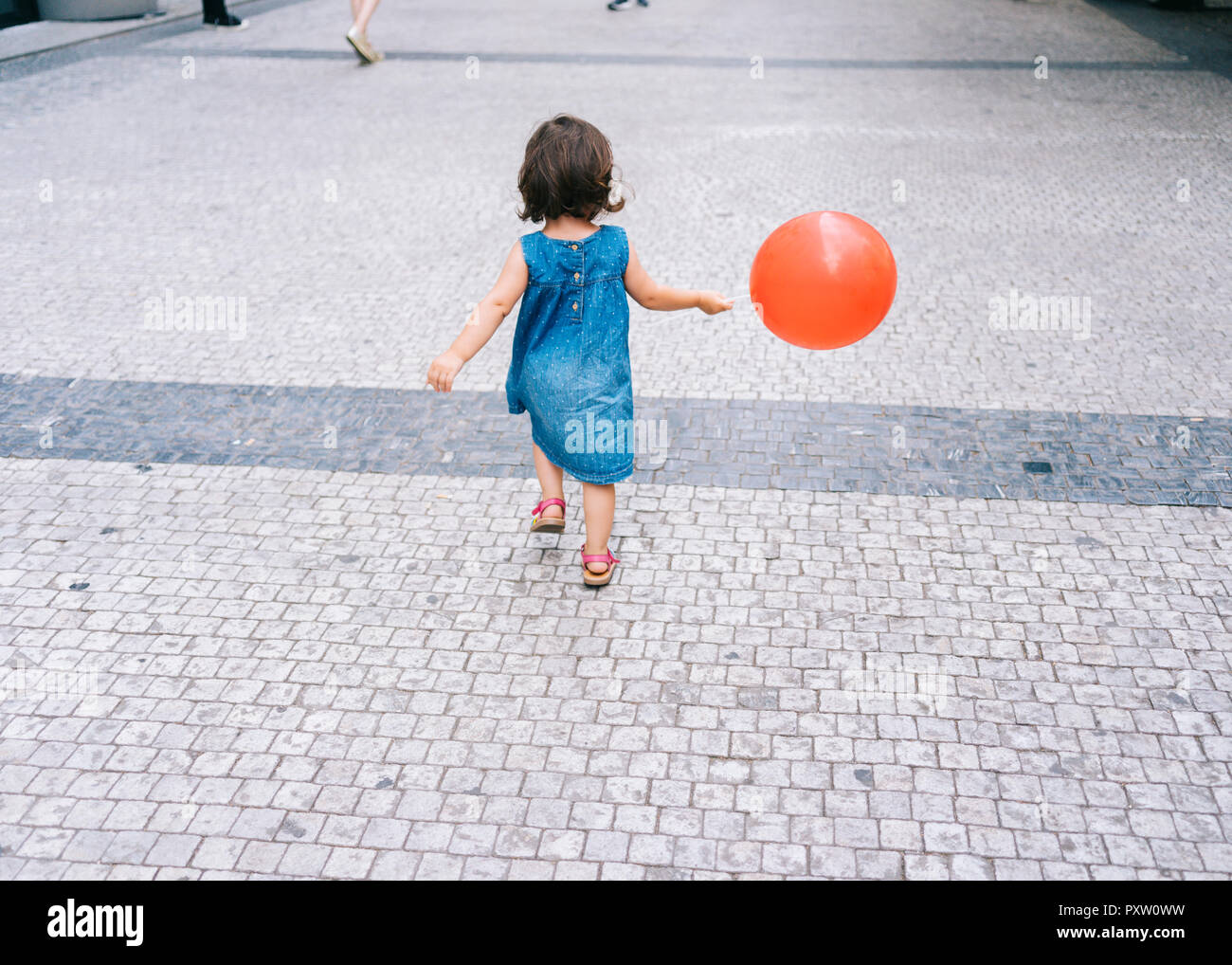 Vue arrière de baby girl with red balloon, marcher sur la chaussée Banque D'Images