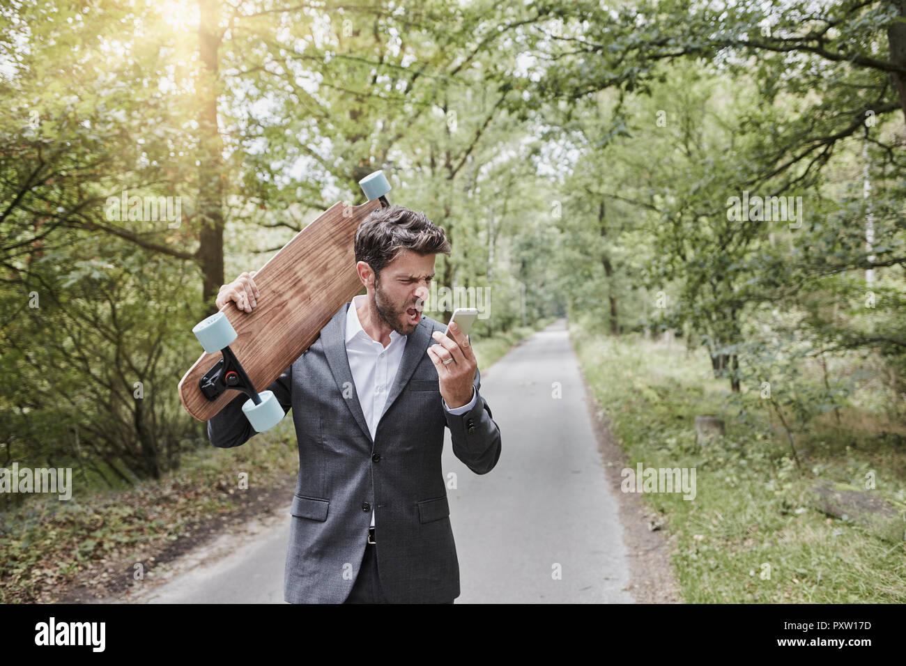 Angry businessman with skateboard smartphone criait on rural road Banque D'Images