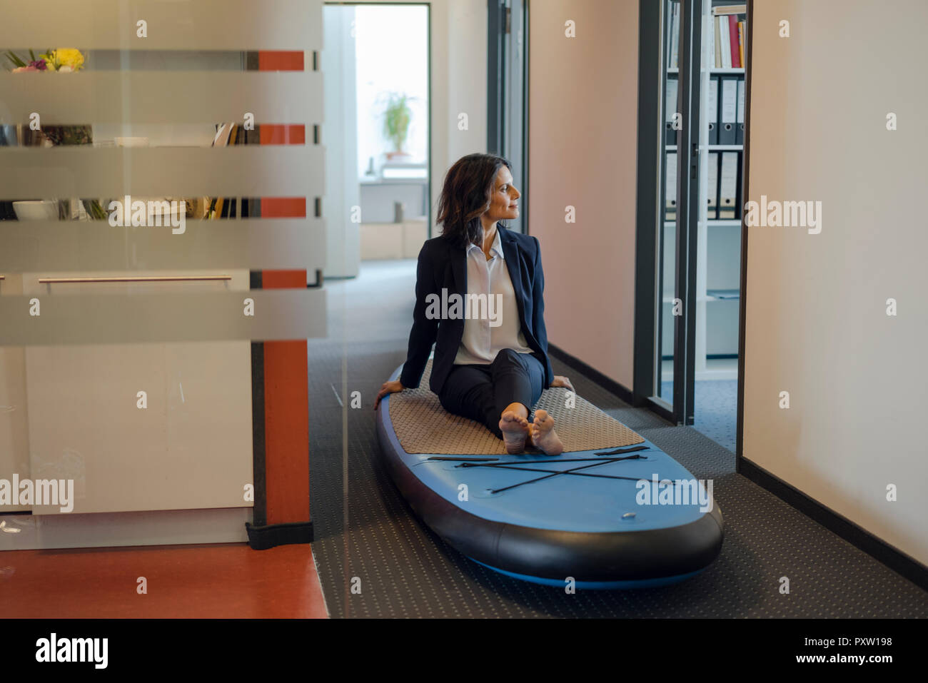 Businesswoman sitting on paddle board, daydreaming in office Banque D'Images