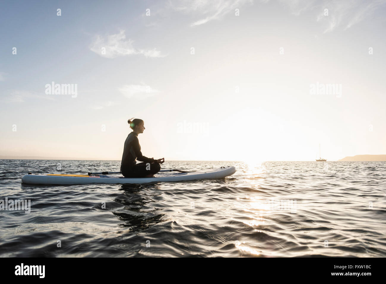 Jeune femme méditant sur paddleboard au coucher du soleil Banque D'Images