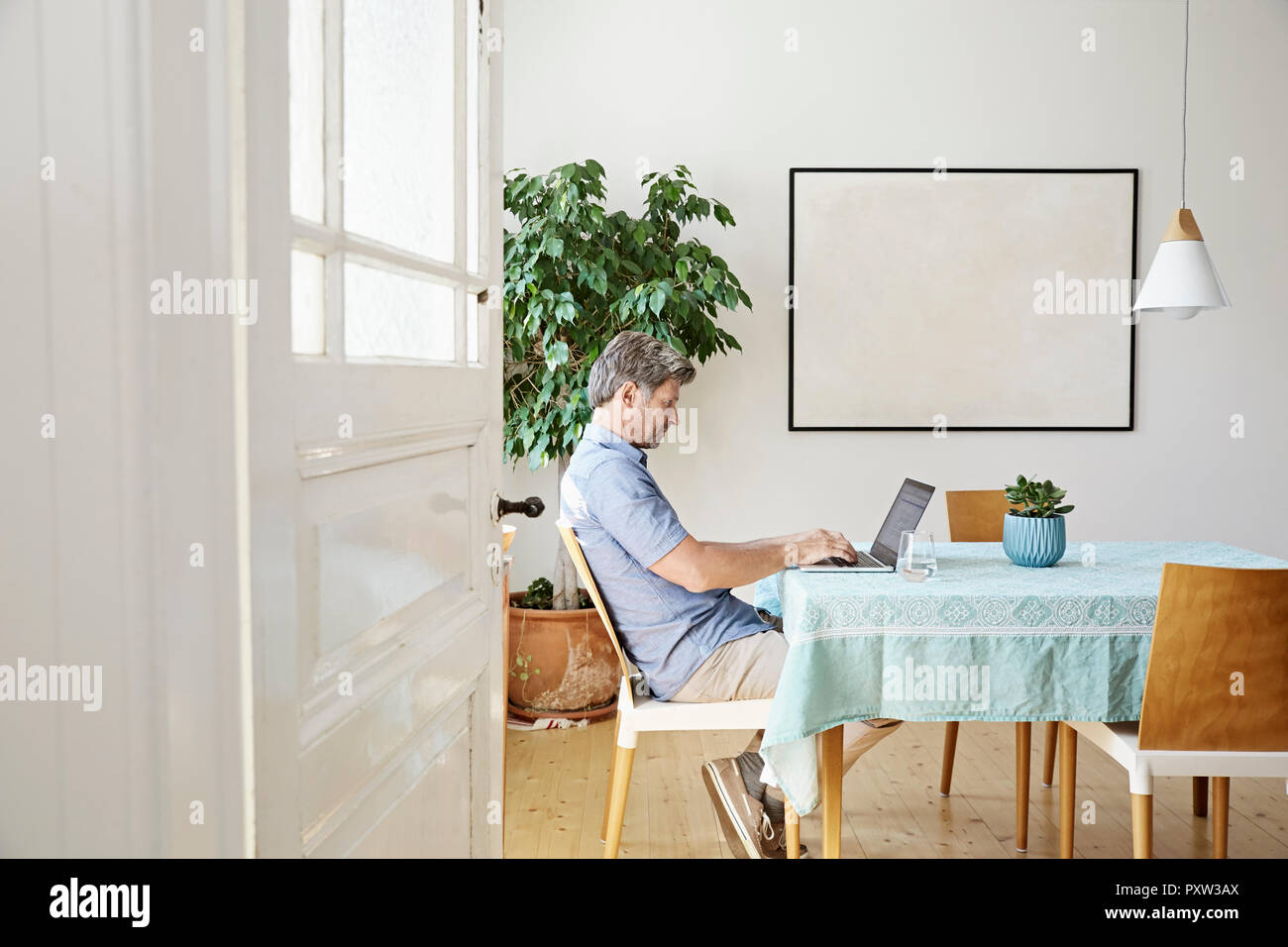 Homme mûr à la maison assis à table, using laptop Banque D'Images