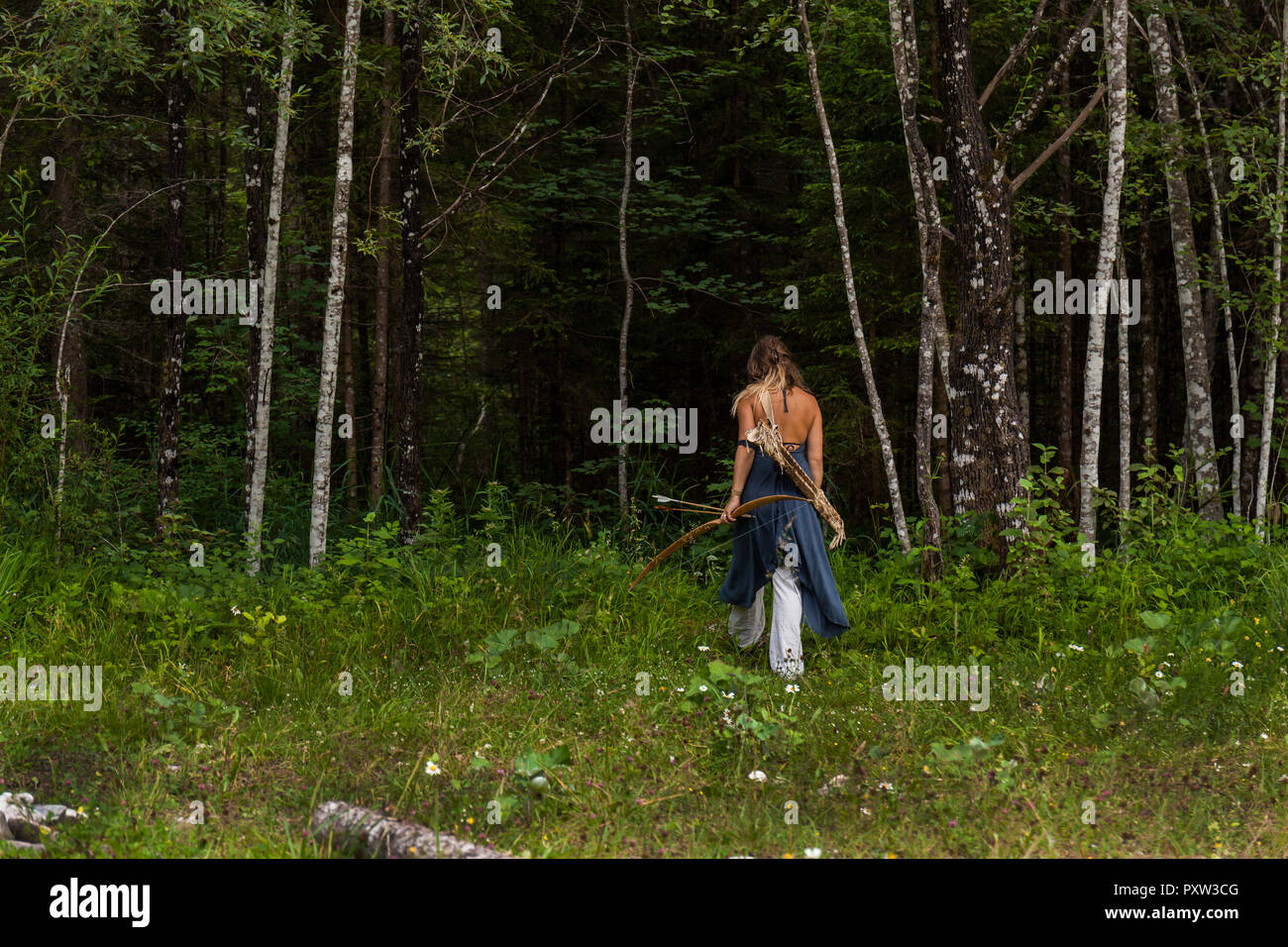 Vue arrière de la femme marchant dans une forêt avec arc et flèche Banque D'Images