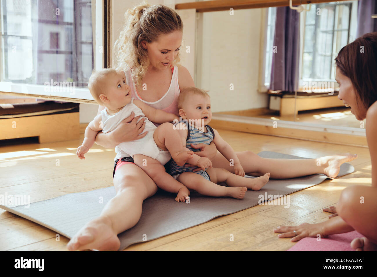 Mère avec des lits bébés assis sur un tapis de yoga Banque D'Images