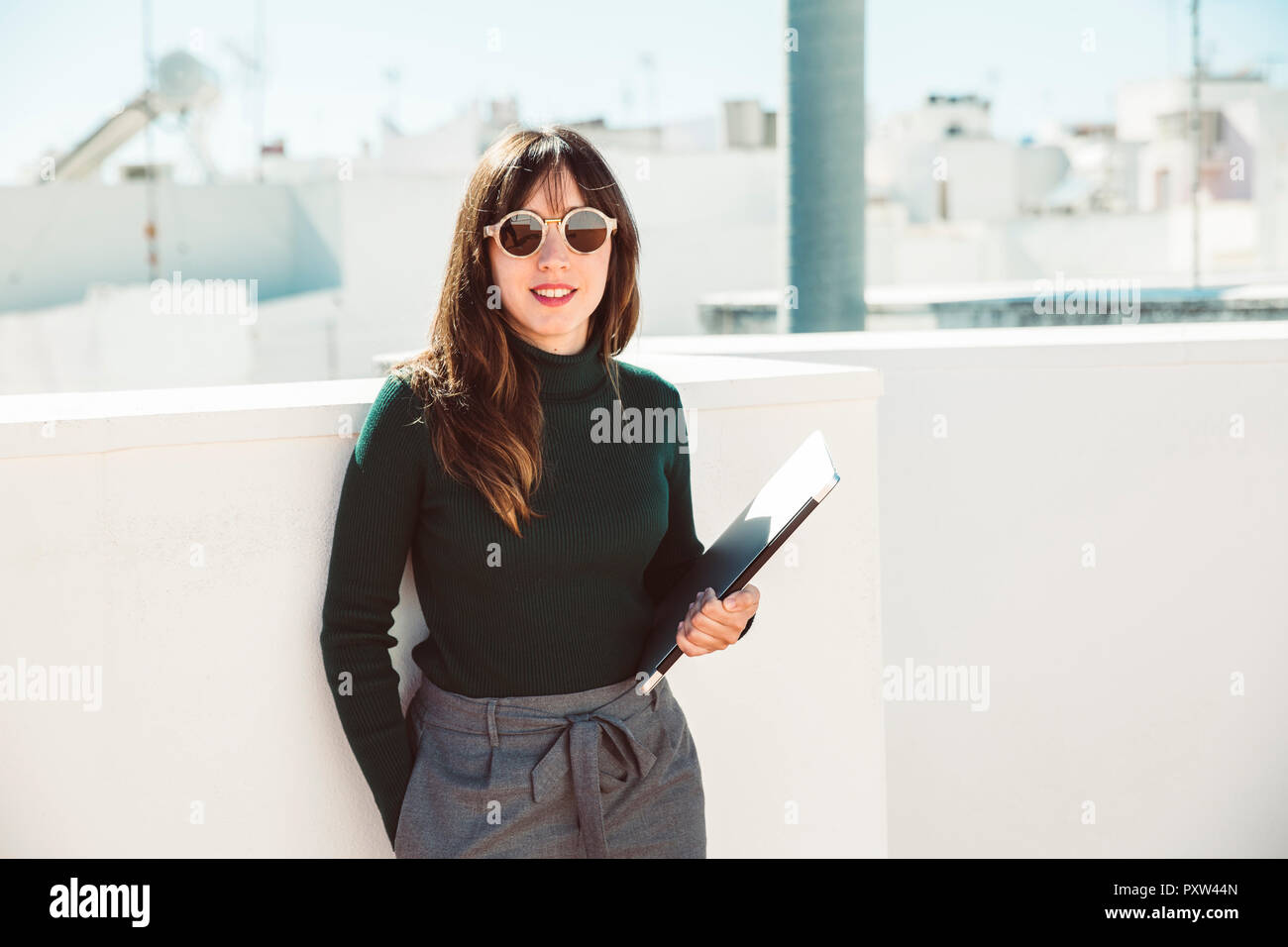 Avec des lunettes de soleil femme debout sur toit, holding laptop Banque D'Images