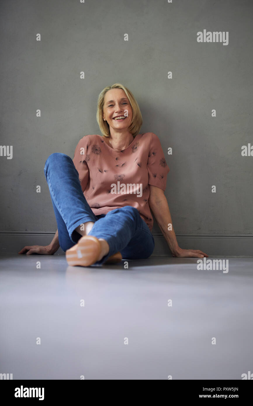 Le Portrait of smiling mature woman à la maison assis sur le plancher Banque D'Images