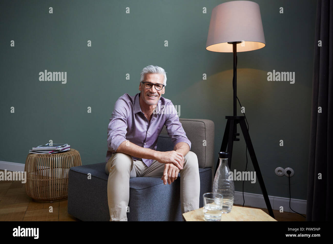 Portrait of smiling mature homme assis sur un fauteuil à la maison Banque D'Images