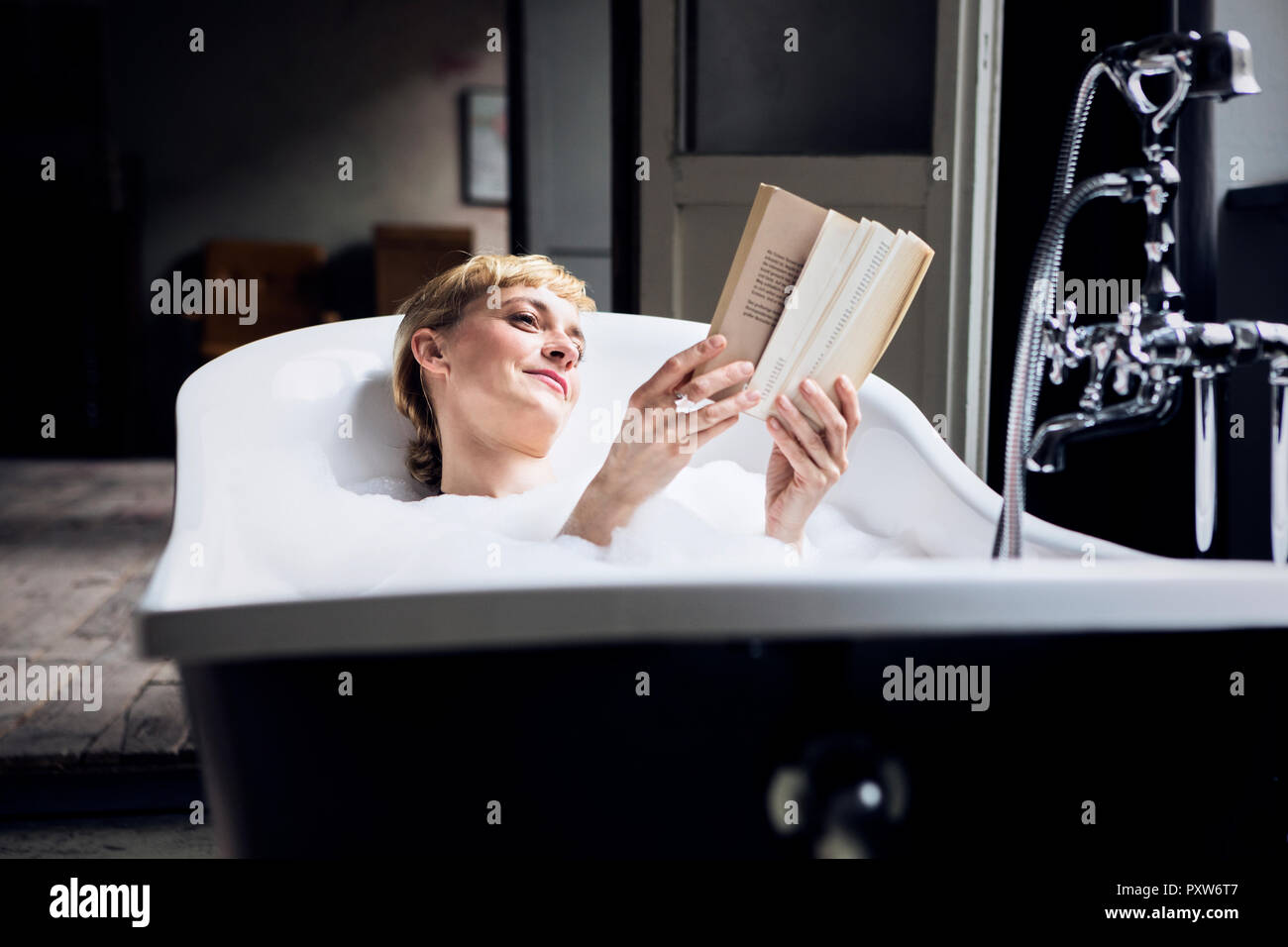 Portrait de femme détendue en prenant un bain de mousse dans un loft de la lecture d'un livre Banque D'Images