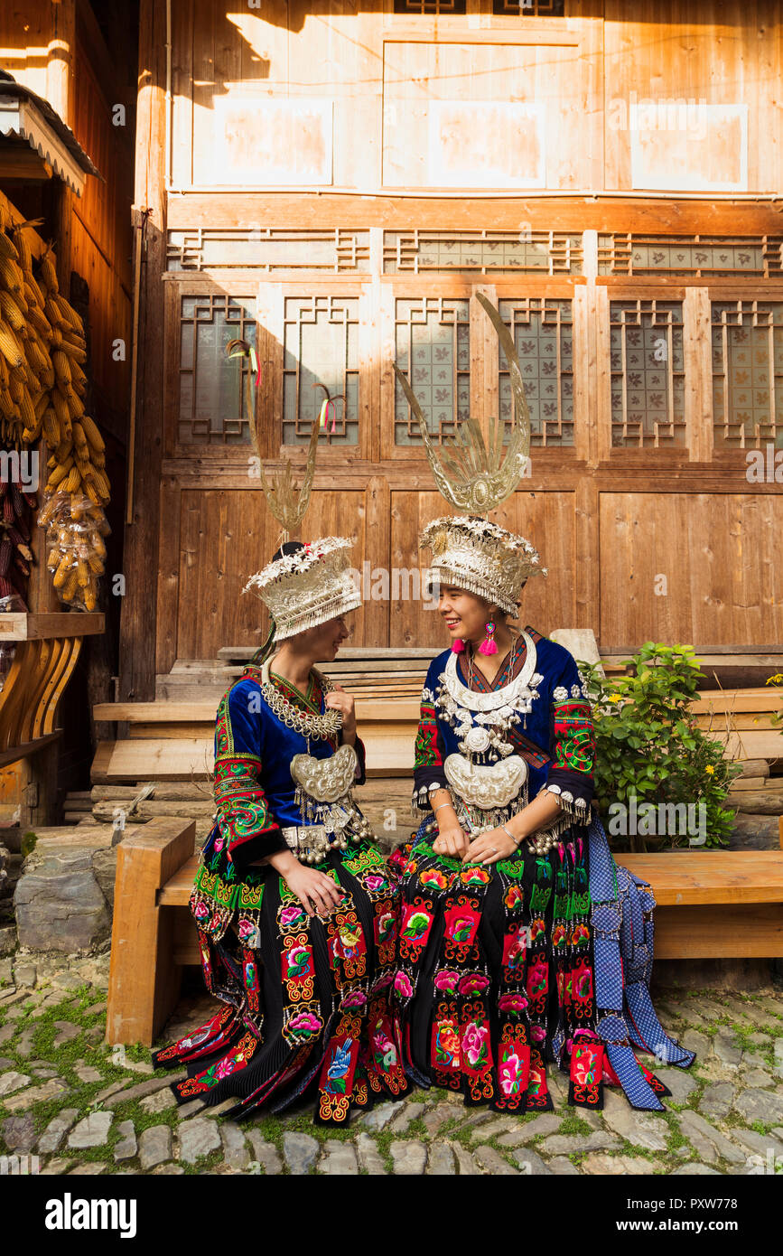 La Chine, Guizhou, deux jeunes femmes Miao souriant portant des vêtements traditionnels et coiffures Banque D'Images