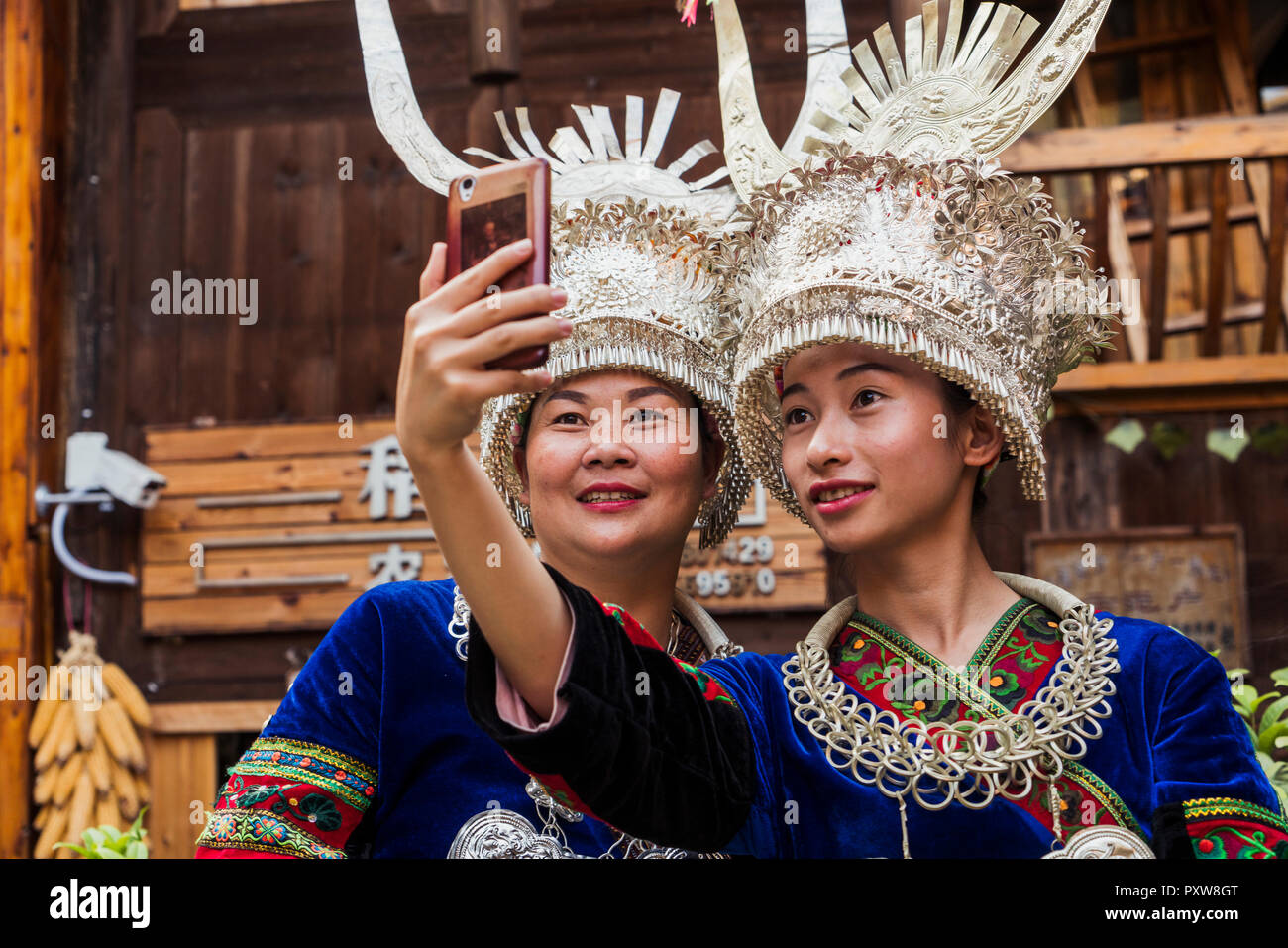 La Chine, Guizhou, deux femmes Miao portant des vêtements traditionnels et coiffures en tenant un smartphone avec selfies Banque D'Images