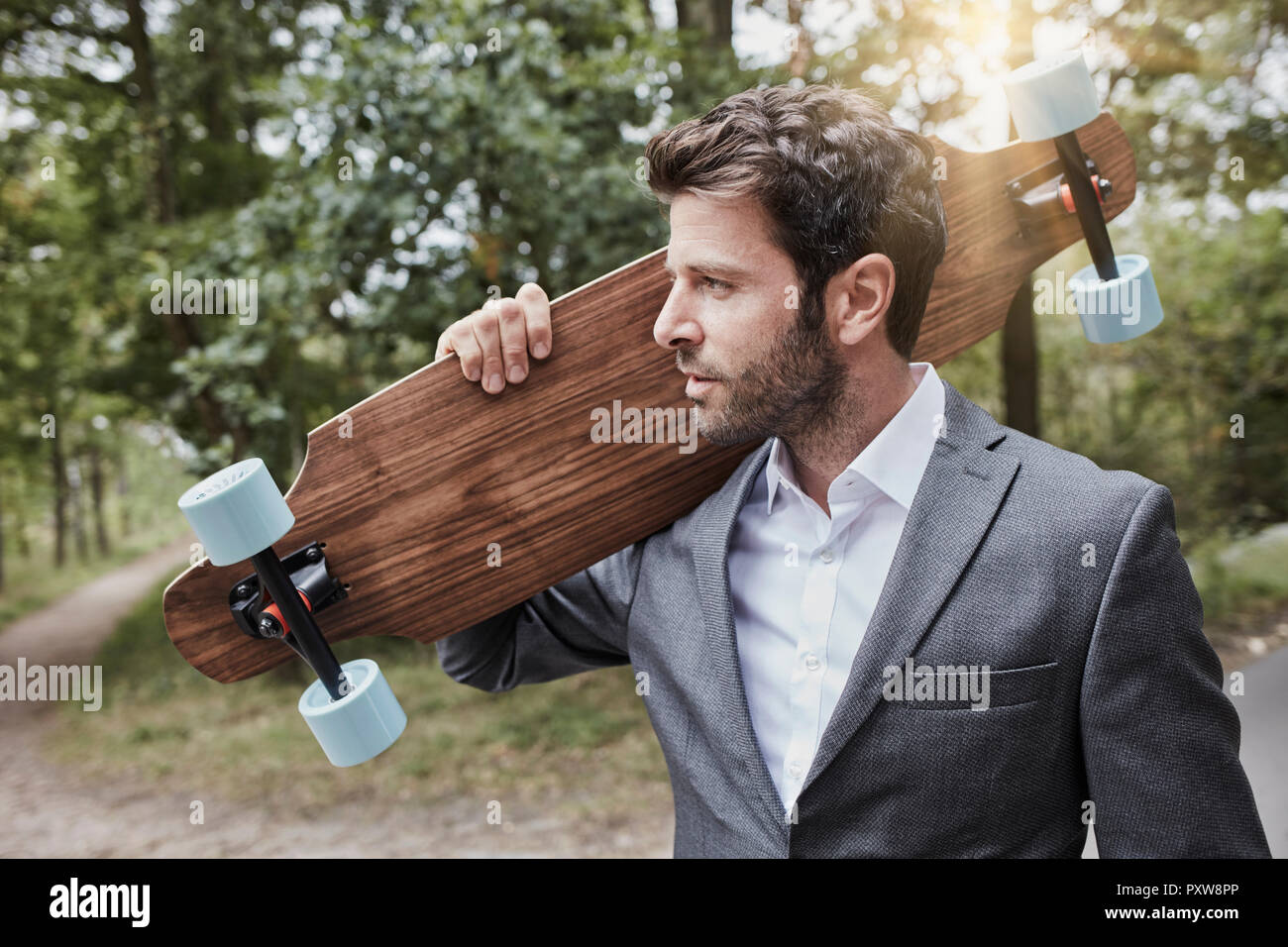 Portrait of businessman carrying skateboard on rural road Banque D'Images