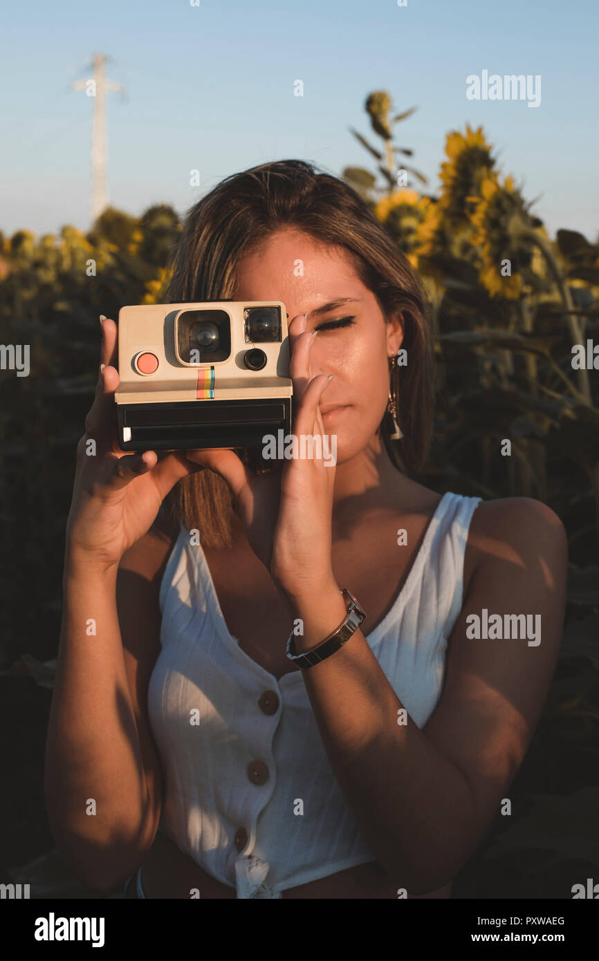 Jeune femme dans un champ de tournesols pour prendre des photos avec un appareil photo instantané Banque D'Images