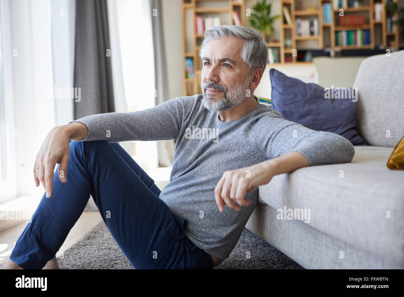 Homme mûr assis sur le plancher de son salon à la fenêtre de Banque D'Images