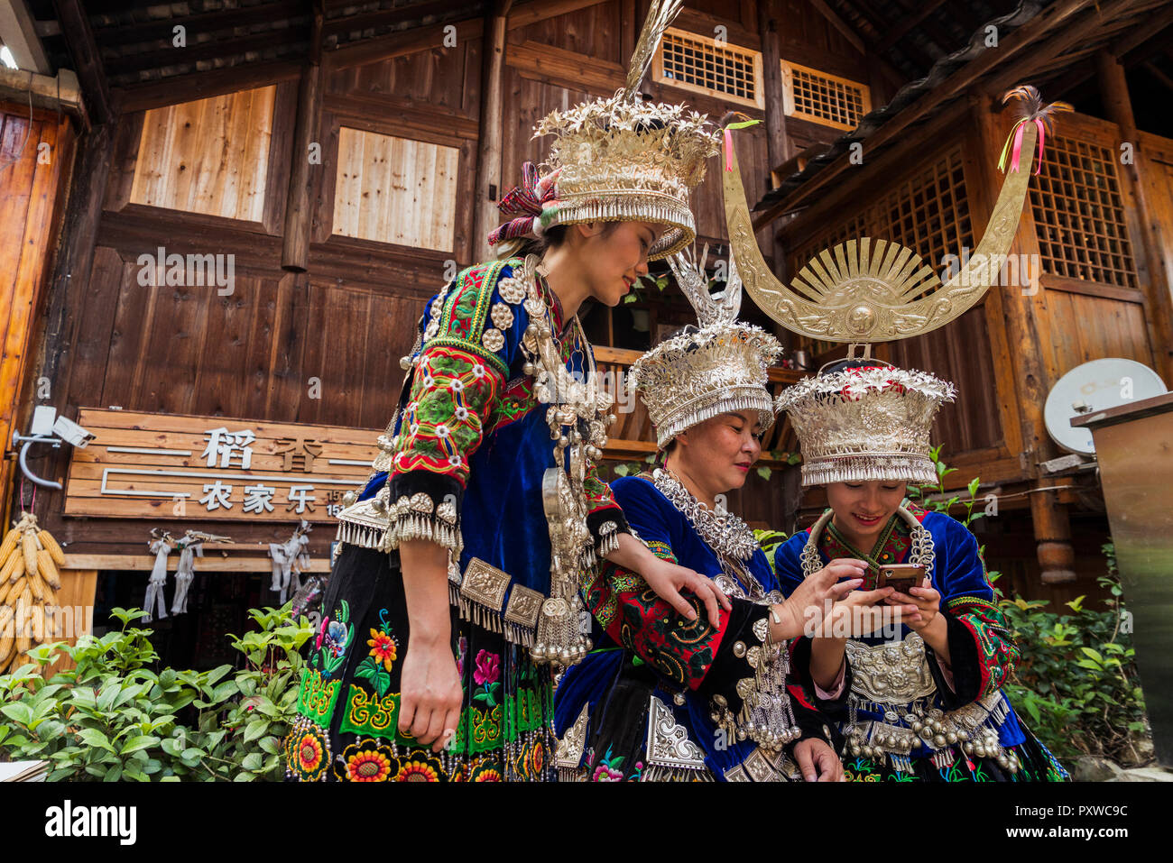 La Chine, Guizhou, trois femmes Miao portant des vêtements traditionnels et coiffures using cell phone Banque D'Images