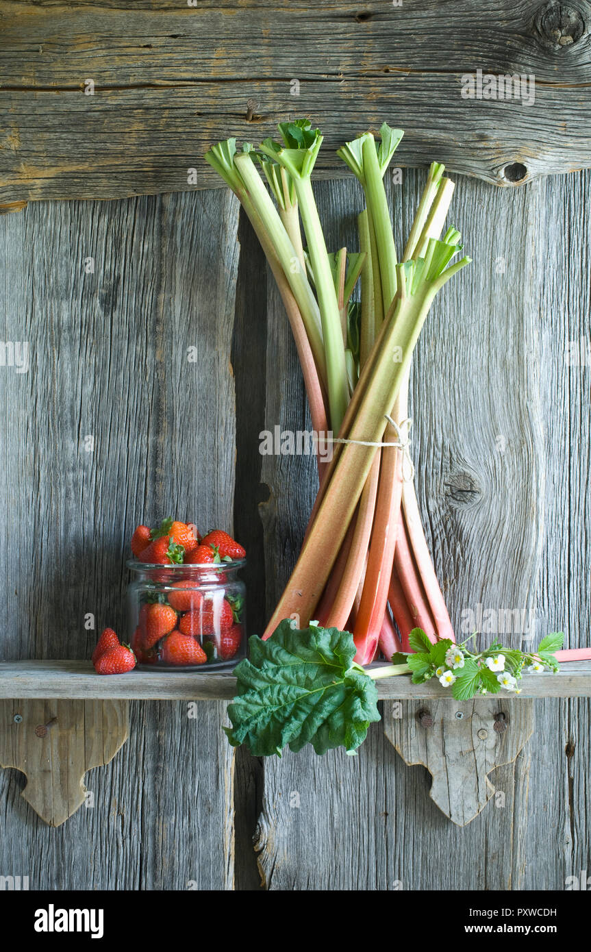 Bouquet de tiges de rhubarbe et fraises dans un verre sur crémaillère Banque D'Images