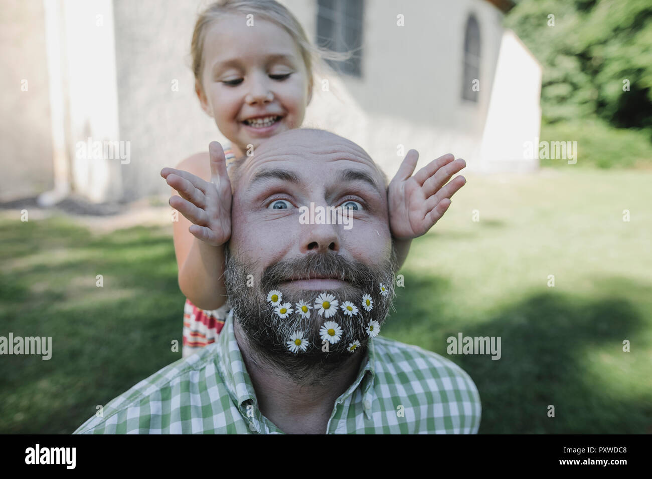 Portrait of mature man with daisies dans sa barbe en jouant avec ma petite fille dans le jardin Banque D'Images
