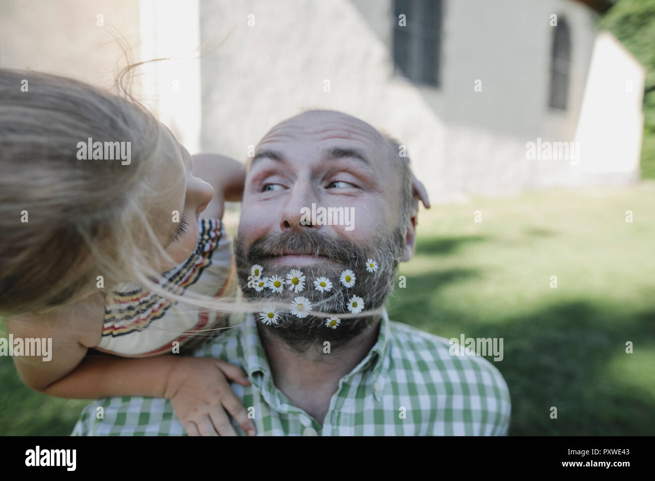 Portrait of smiling Young man with daisies dans sa barbe en jouant avec ma petite fille dans le jardin Banque D'Images