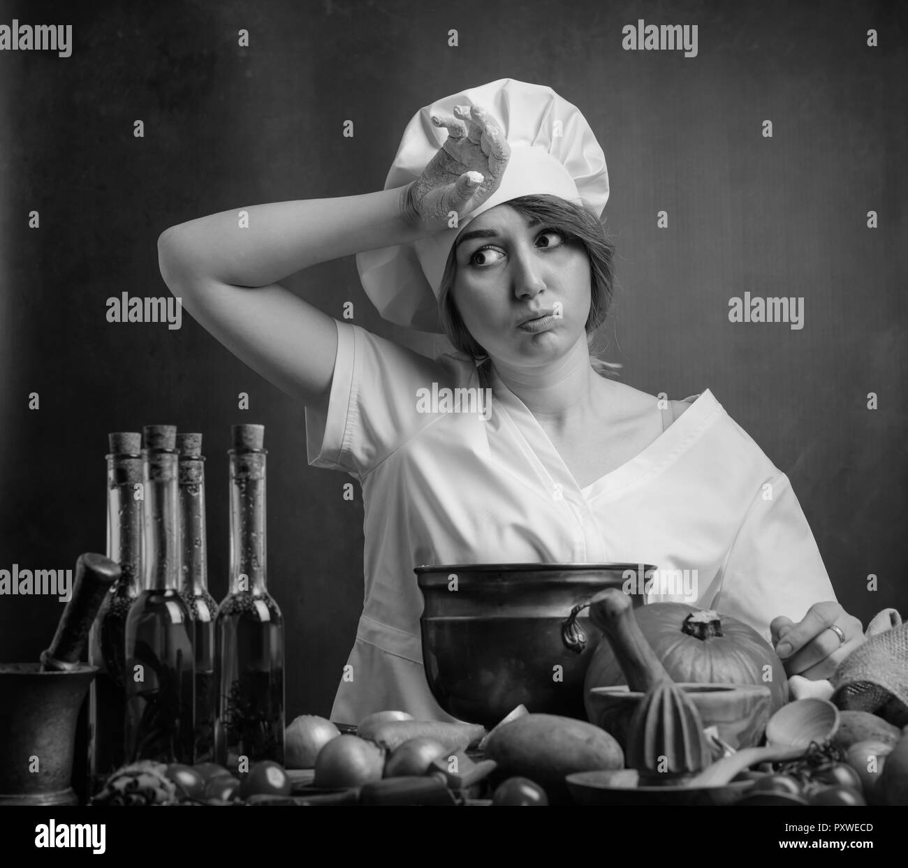 Assez jeune belle fille dans un uniforme de chef. Sur une table divers ustensiles de cuisine et les légumes. Banque D'Images