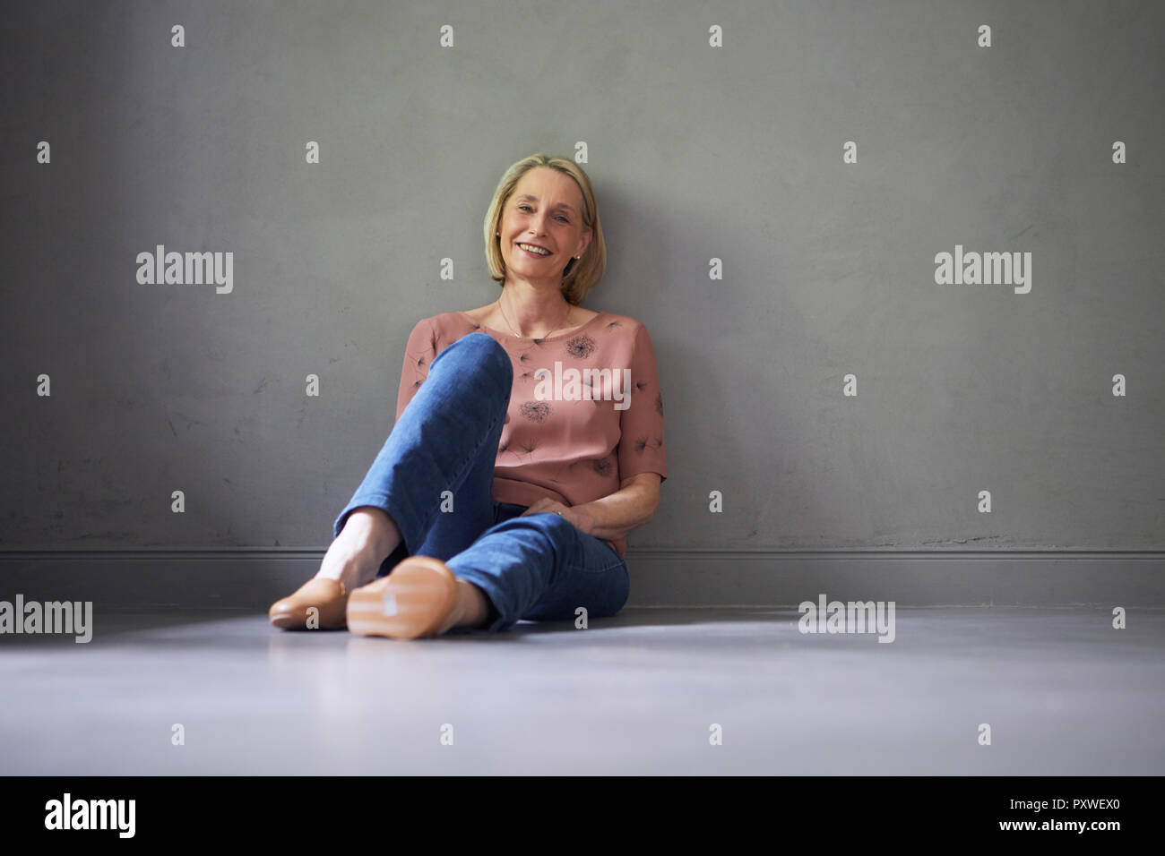 Le Portrait of smiling mature woman à la maison assis sur le plancher Banque D'Images